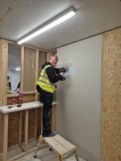 fixing plasterboard to a framed wall using a drill during dry lining training