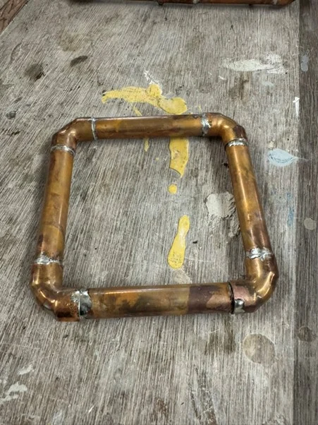 Square copper pipe frame with soldered joints on a workshop floor