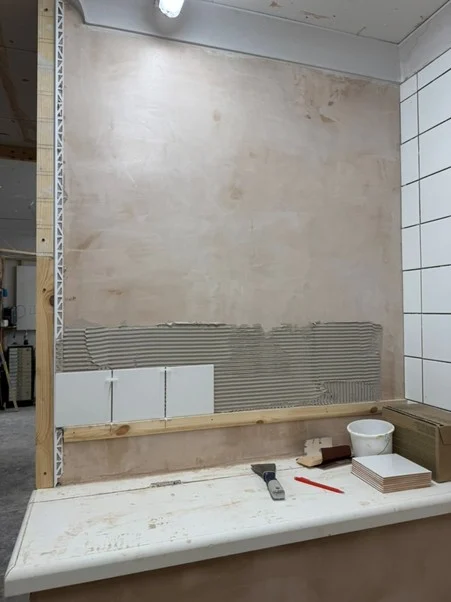 First row of wall tiles set into adhesive on a practice wall